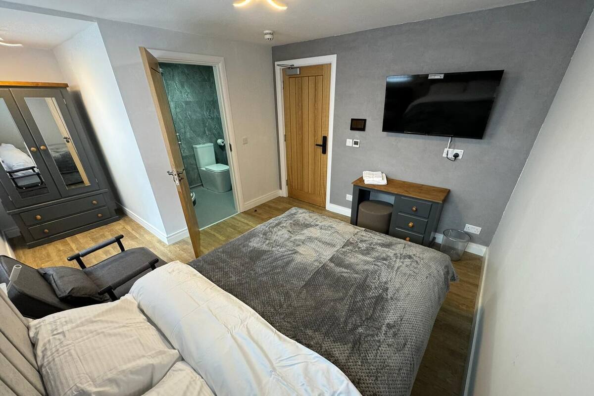 A modern bedroom with a large bed, a TV mounted on the wall, and a wardrobe.