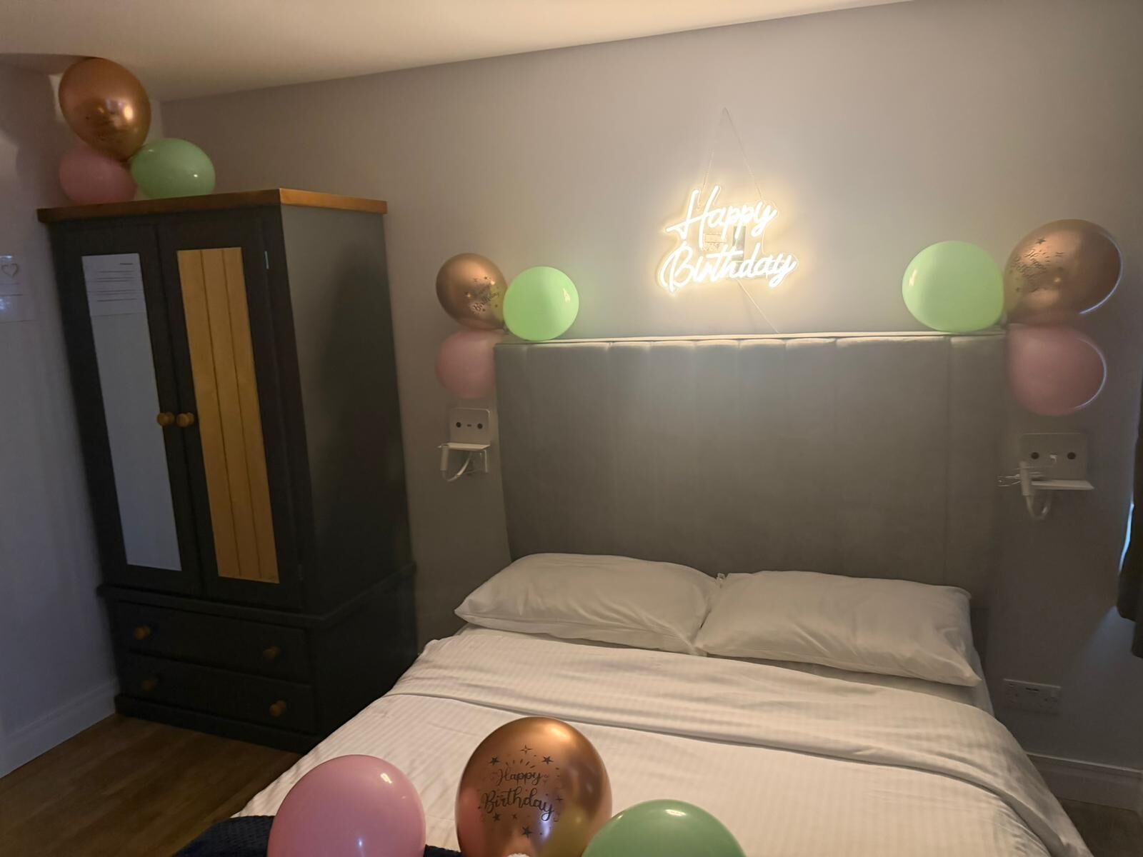 A bedroom with a bed, a neon 'Happy Birthday' sign, and balloons.