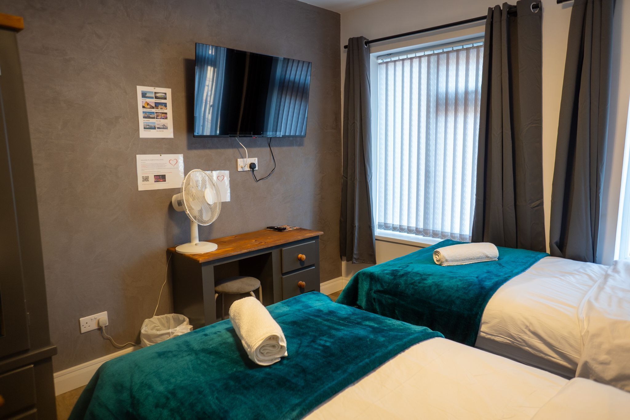 A hotel room with two beds, a TV, a desk with a chair, and a window with curtains.