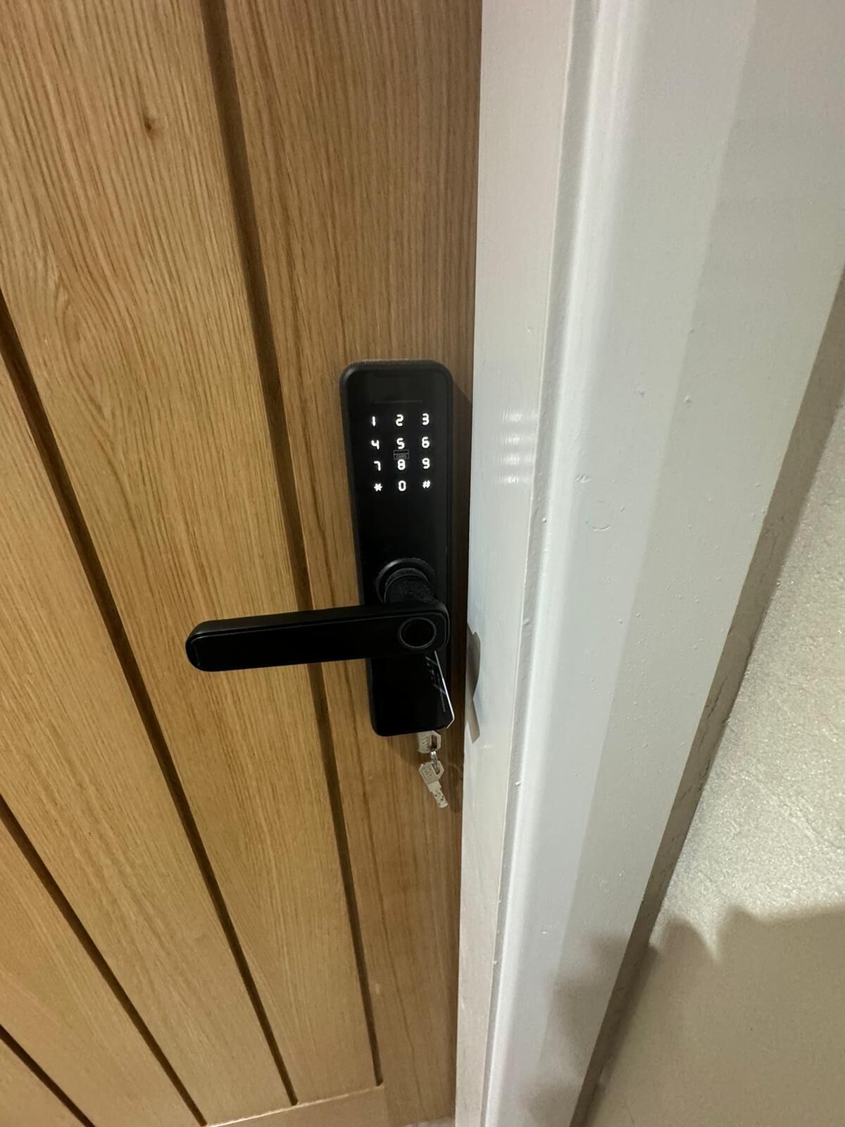 En trædør med en sort elektronisk keypad-lås og en nøgle i låset.
