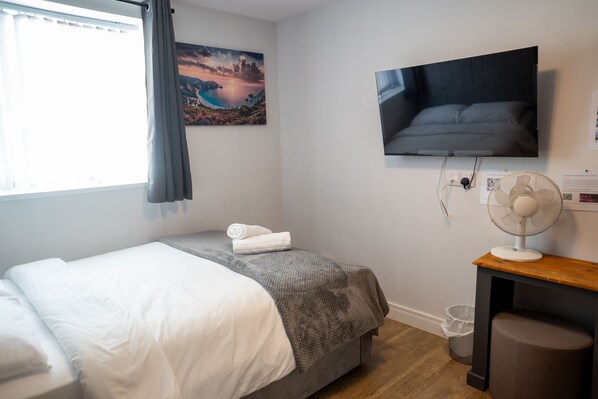 A bedroom with a bed, a TV mounted on the wall, a fan, and a painting. - Heart of Hull Hotel (Hull)