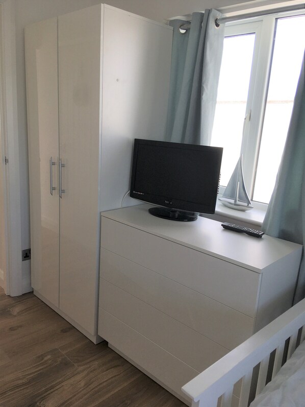 Un dormitorio con cama, escritorio con monitor de computadora y ventana con cortinas.