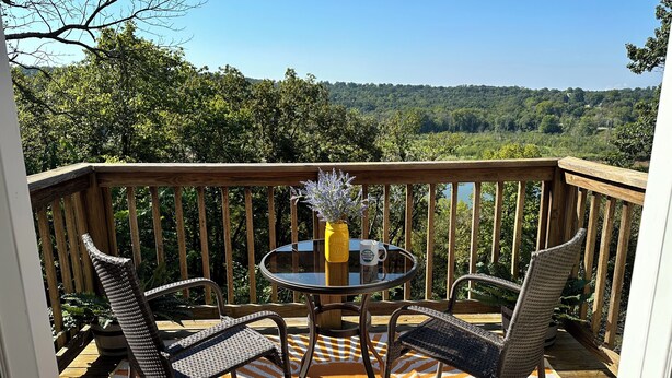A wooden deck with two wicker chairs and a glass table, a yellow vase with flowers, and a mug. - Lake Views! Little Bell Bungalow Charmer, Backyard, Game Room, Foosball (Forsyth)