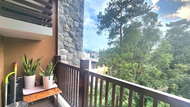 Un balcón con pared de piedra, banca de madera y plantas en macetas.