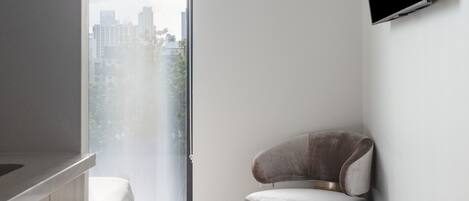 A modern bedroom with a bed, a round chair, a TV, and a city view.