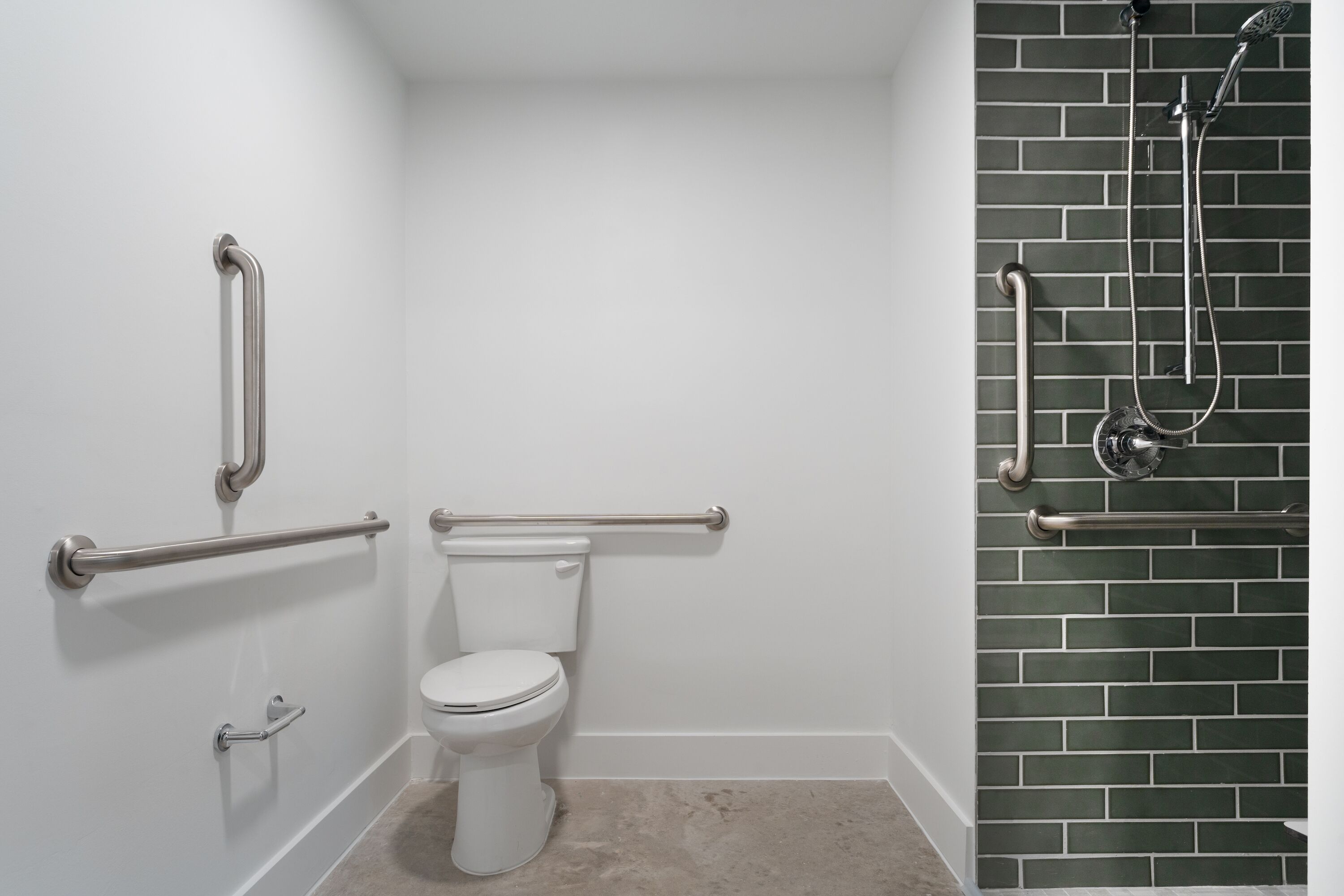 A bathroom with a white toilet, a shower with a glass door, and a green brick wall.