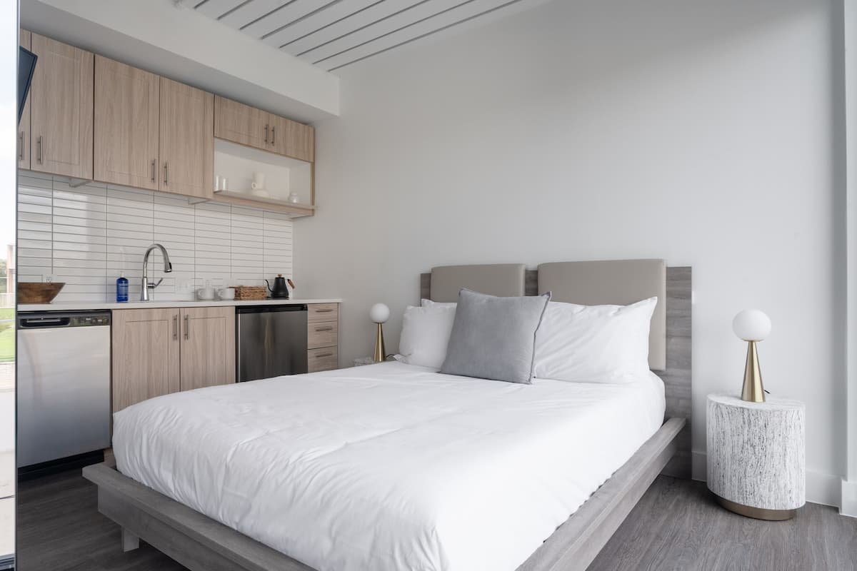 Un dormitorio moderno con una cama grande, mesitas de noche, un armario empotrado y una pequeña cocina.