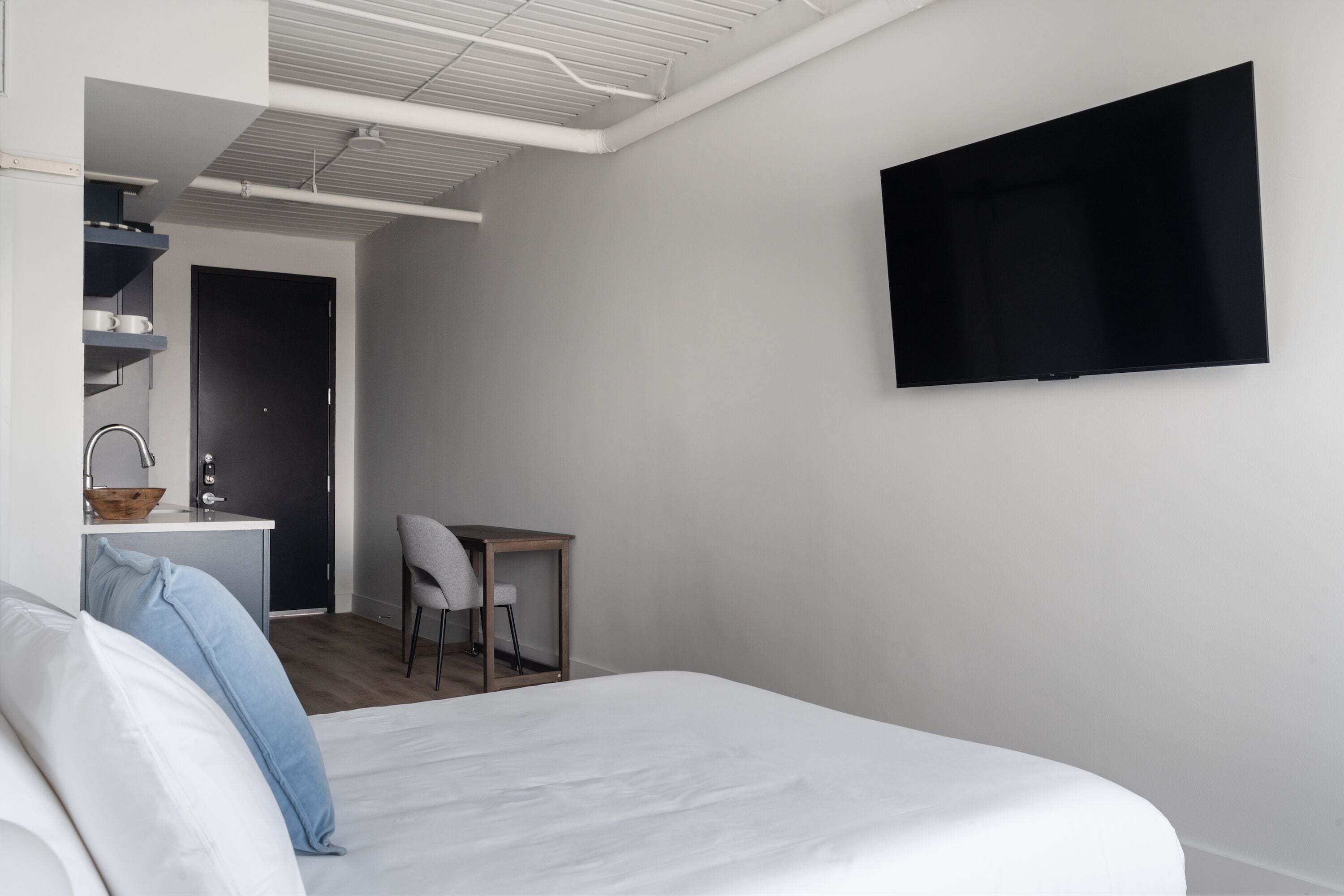 A modern bedroom with a bed, a desk, and a TV mounted on the wall.