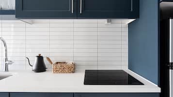 Una cocina moderna con armarios azul oscuro, encimera blanca, placa de cocina por inducción negra y hervidor de acero inoxidable.