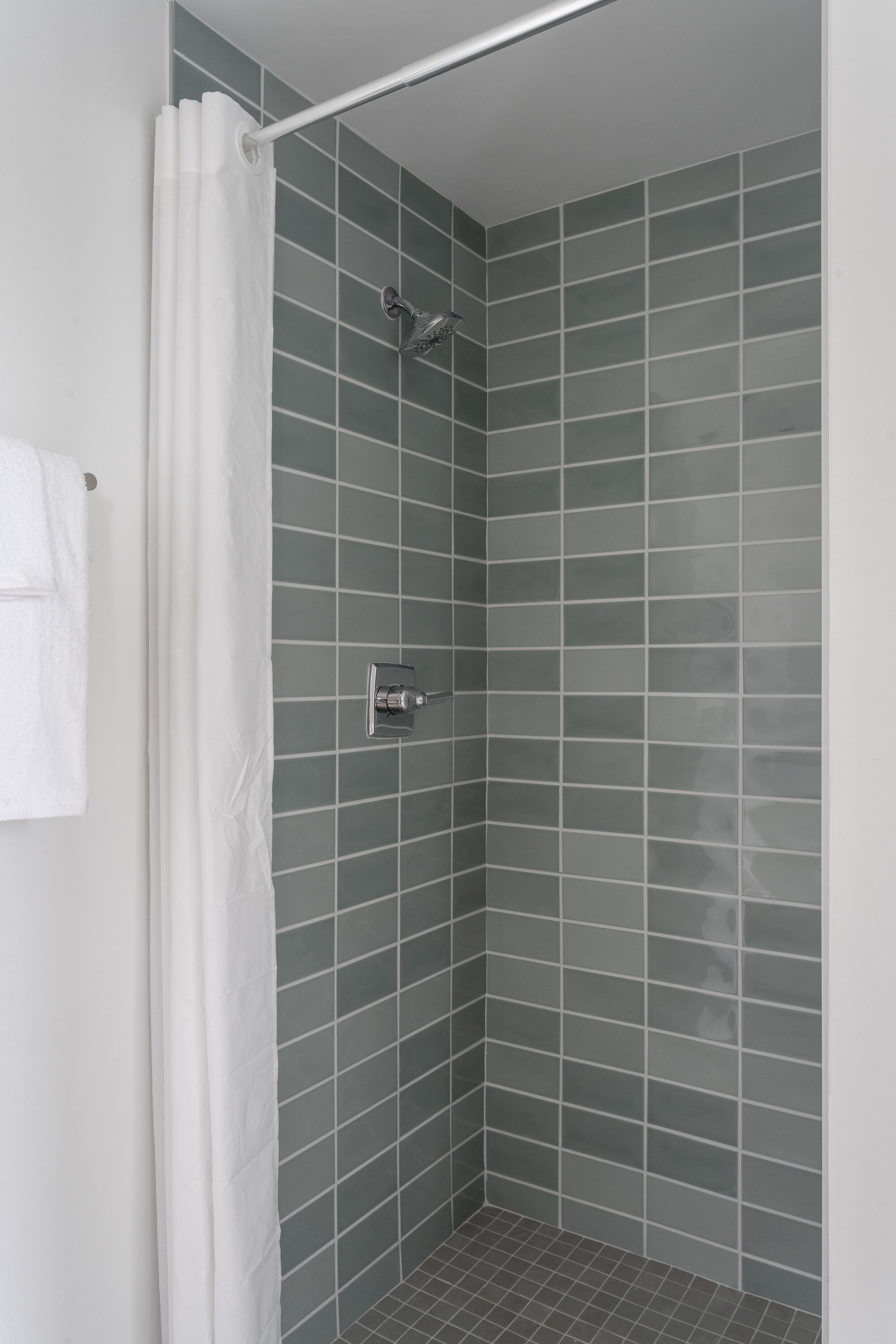A shower area with a white curtain, a showerhead, and a tiled wall.