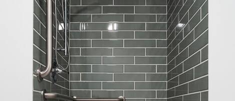 Un petit espace de douche fermé, équipé d’une barre d’appui en métal, d’un pommeau de douche à main et d’un banc.