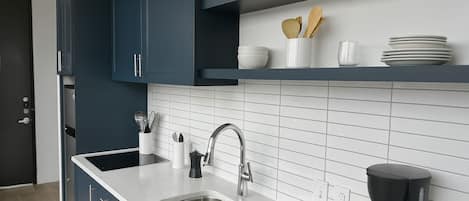 A modern kitchen with dark blue cabinets, a white countertop, a stainless steel sink, and a coffee maker.
