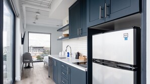 A modern kitchen with dark blue cabinets, a stainless steel refrigerator, and a large window offering a city view. -  Studio Haus East 6th Austin by Kasa (Austin)