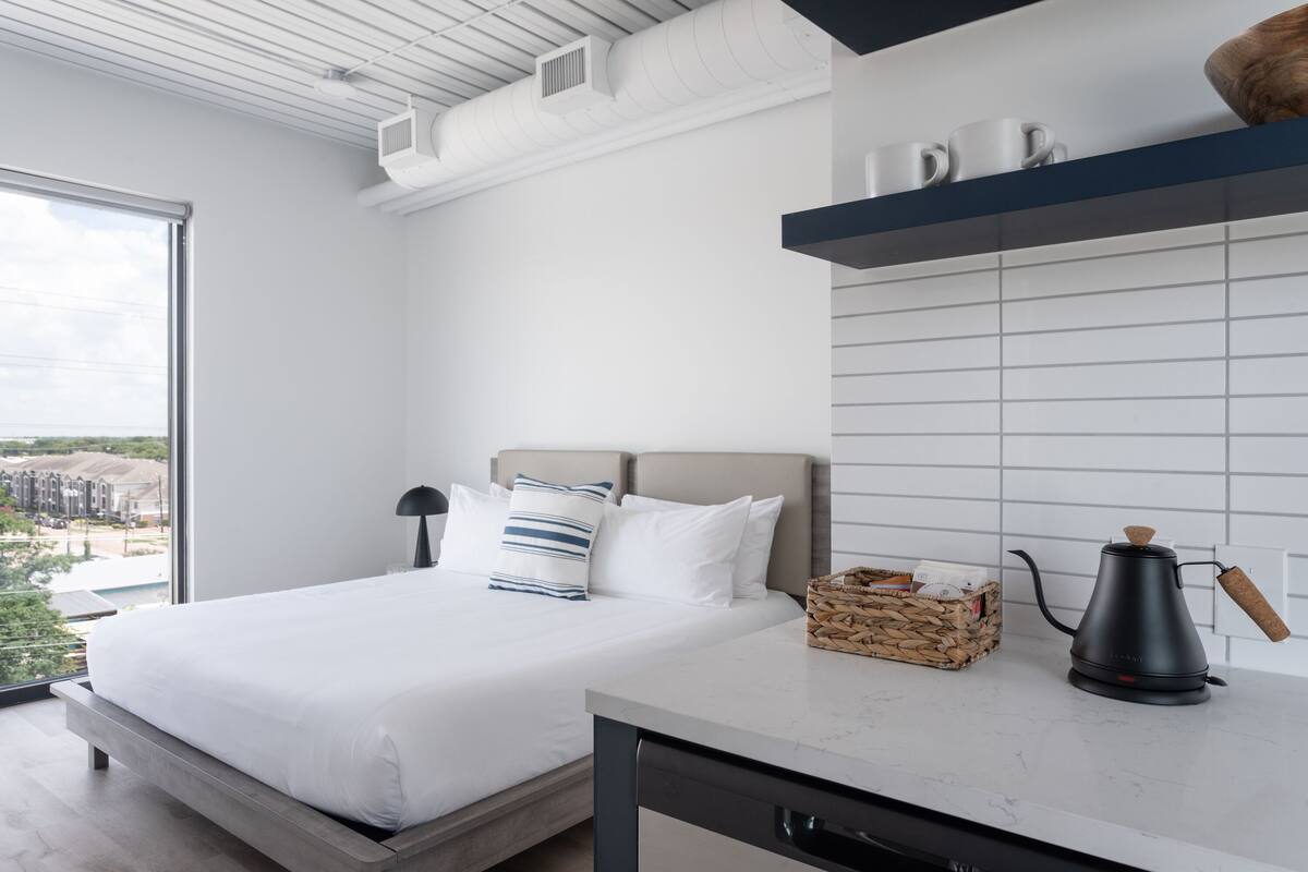 Un dormitorio moderno con una cama grande, una mesita de noche, una cafetera y vistas al exterior.