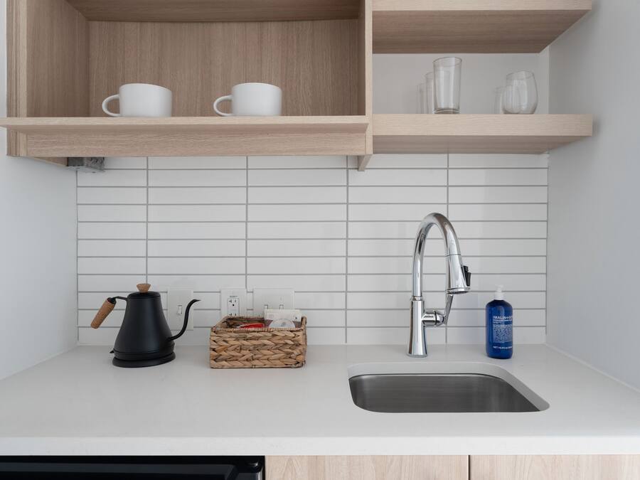 Una cocina moderna con un lavamanos de acero inoxidable, una cafetera y una cesta de objetos sobre la encimera.