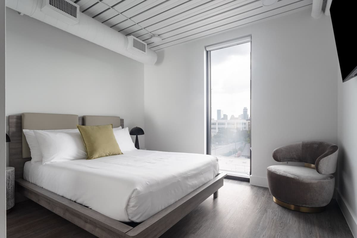 Un dormitorio moderno con una cama grande, una silla y vistas a la ciudad a través de una ventana.