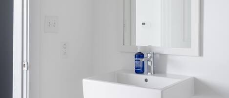 Un baño blanco con lavamanos, espejo y puerta que da a otra habitación.