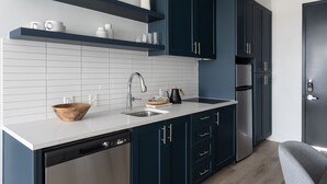 A modern kitchen with dark blue cabinets, white tiles, a stainless steel dishwasher, and a built-in oven. -  Studio Haus East 6th Austin by Kasa (Austin)