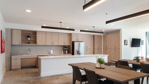 A modern kitchen with wooden cabinets, a central island, and a dining area with a table and chairs. -  Studio Haus East 6th Austin by Kasa (Austin)