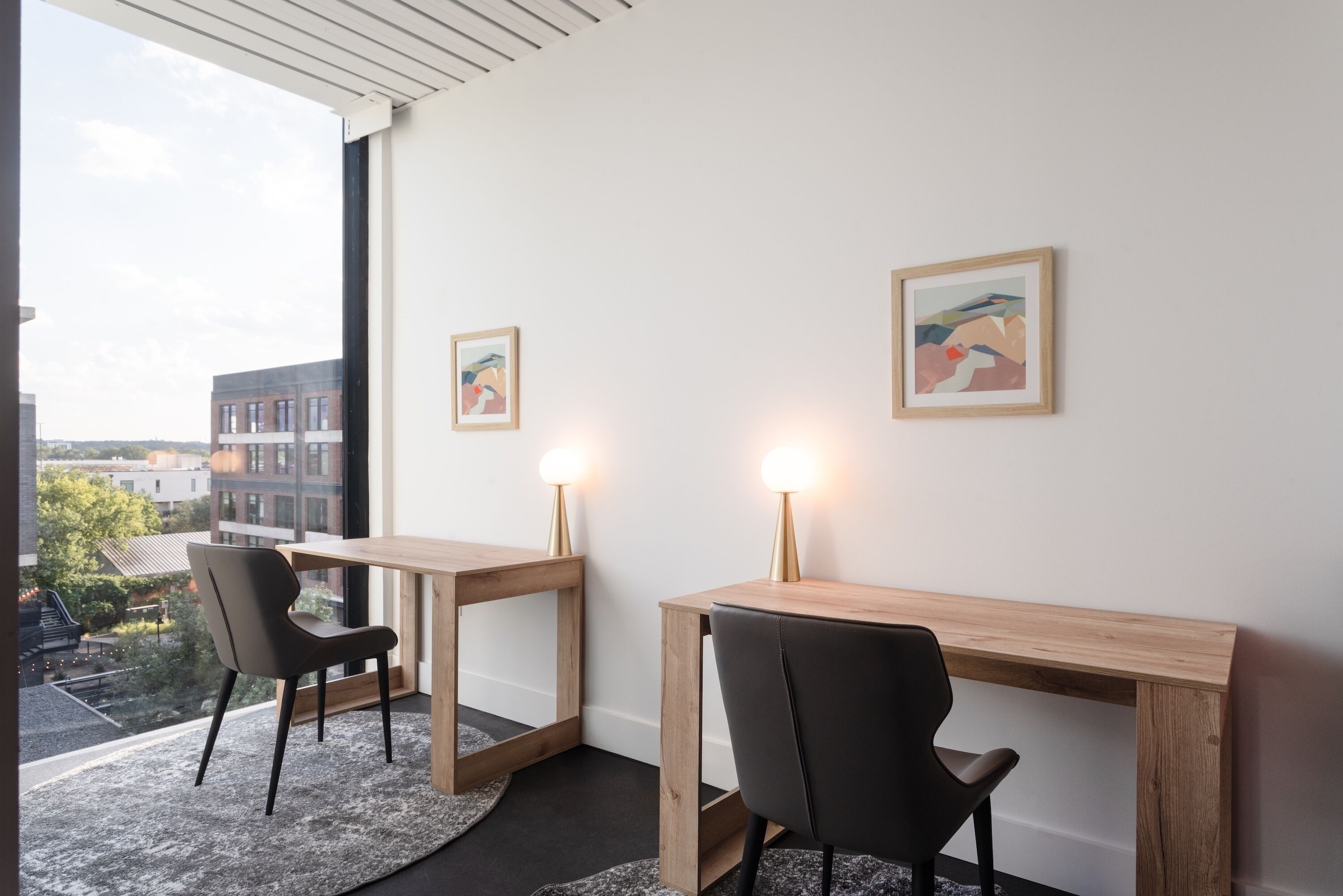 A modern room with two wooden desks, black chairs, and framed artwork on the walls.
