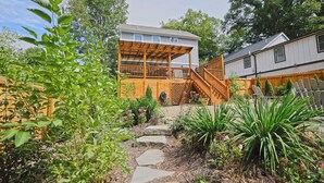 Una casa con terraza de madera, camino de piedra y jardín con diversas plantas.