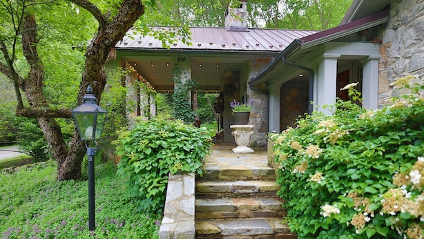 A stone staircase leading to a covered porch with a metal roof, surrounded by lush greenery and a lantern post. - Crab Orchard Estate in Valle Crucis w/ Fireplace (Valle Crucis)