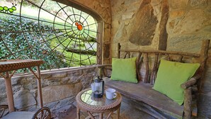 A stone-walled room with a wooden bench, a wicker table, and a glass table with a coffee pot and cup. - Crab Orchard Estate in Valle Crucis w/ Fireplace (Valle Crucis)