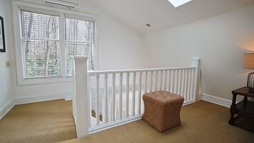 A room with a white railing, a brown ottoman, and a window with blinds.