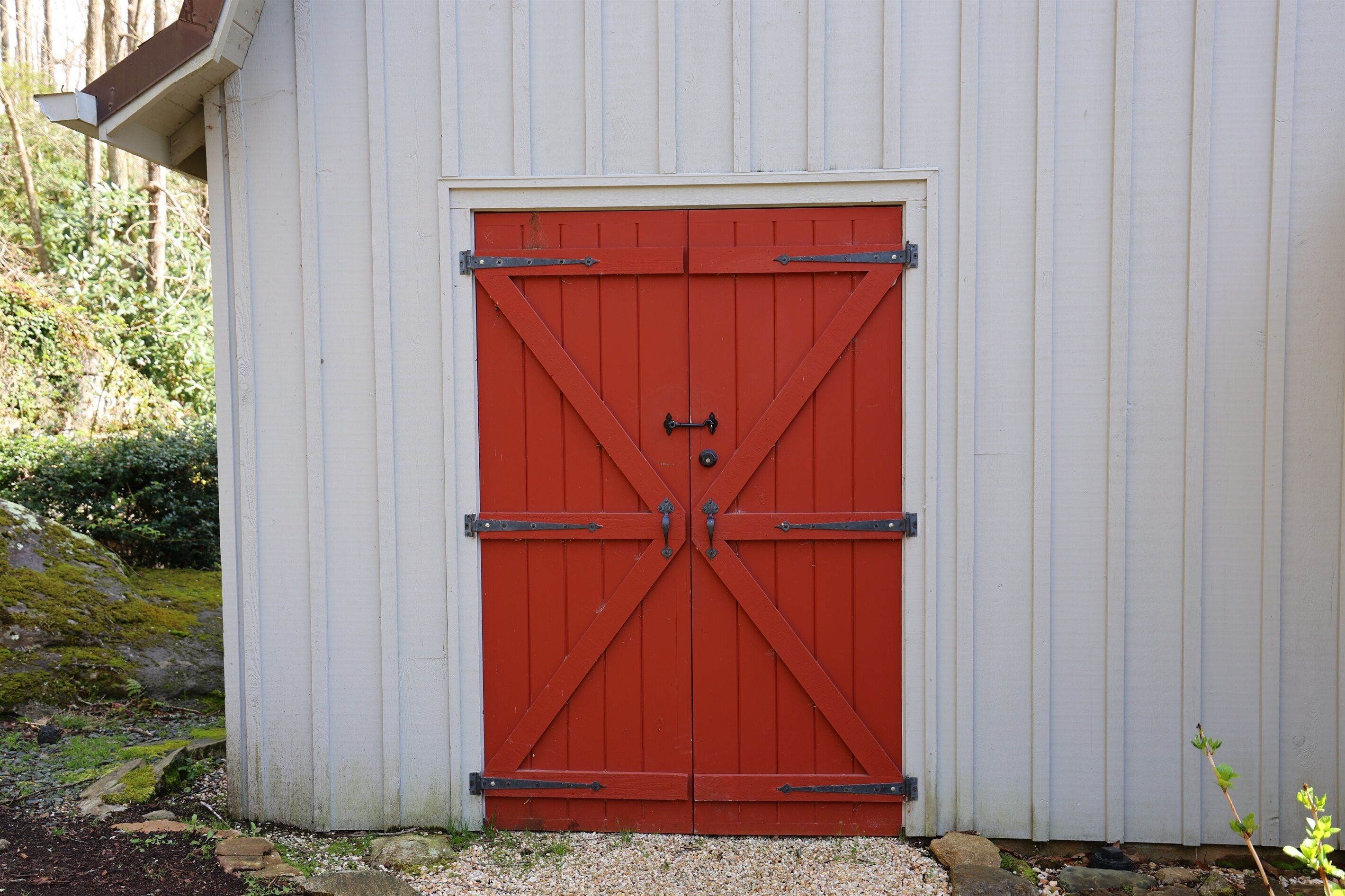 A red barn-style door with metal hinges and a lock, set in a white building with vertical siding.