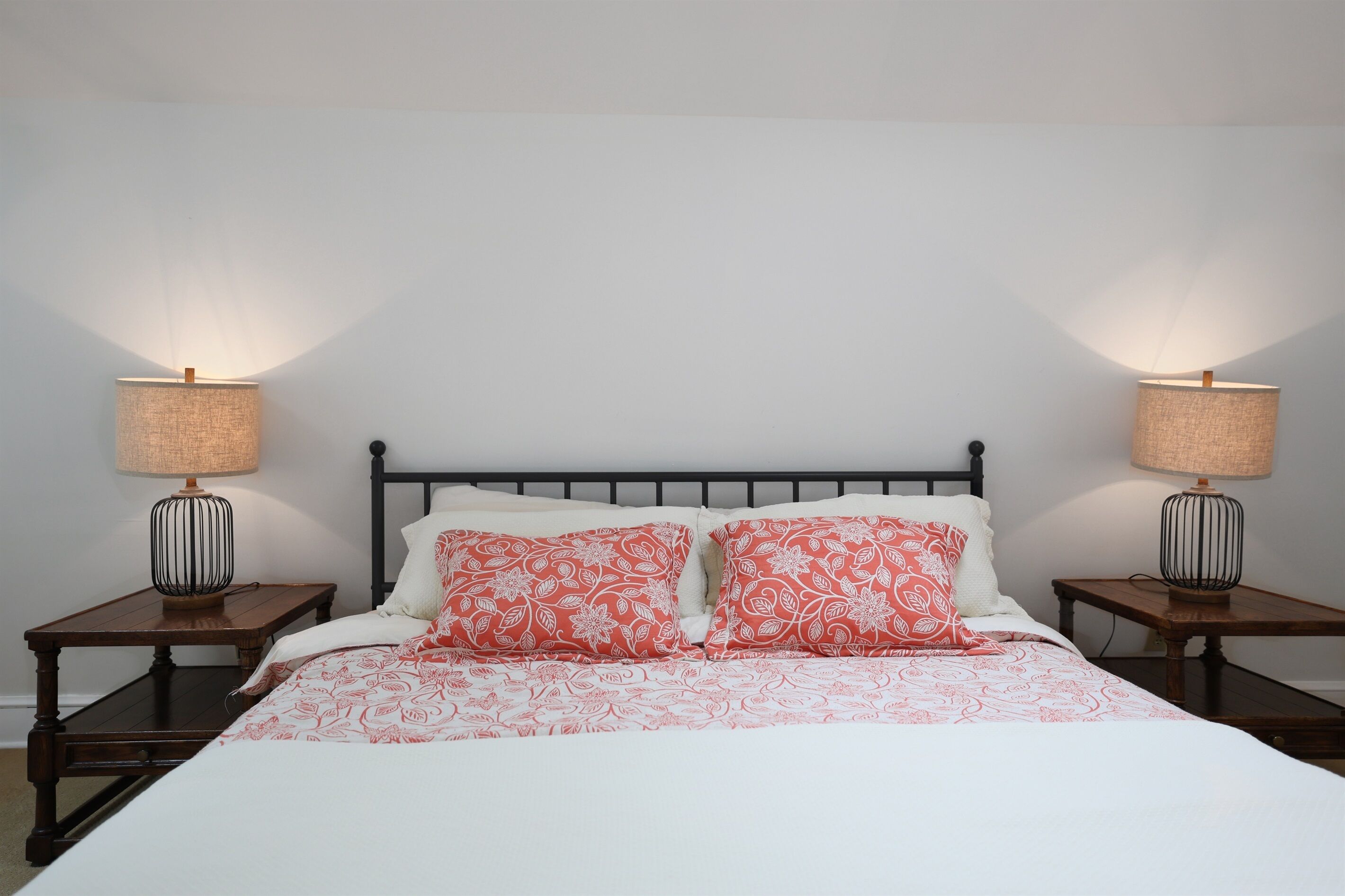 Een bed met een wit en rood beddegoed, aan weerszijden omringd door nachtkastjes met lampen, in een kamer met effen witte muren en een zwart hoofdeinde.