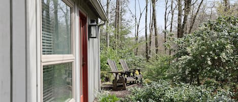 A house with large windows, a red door, and a garden with two Adirondack chairs.