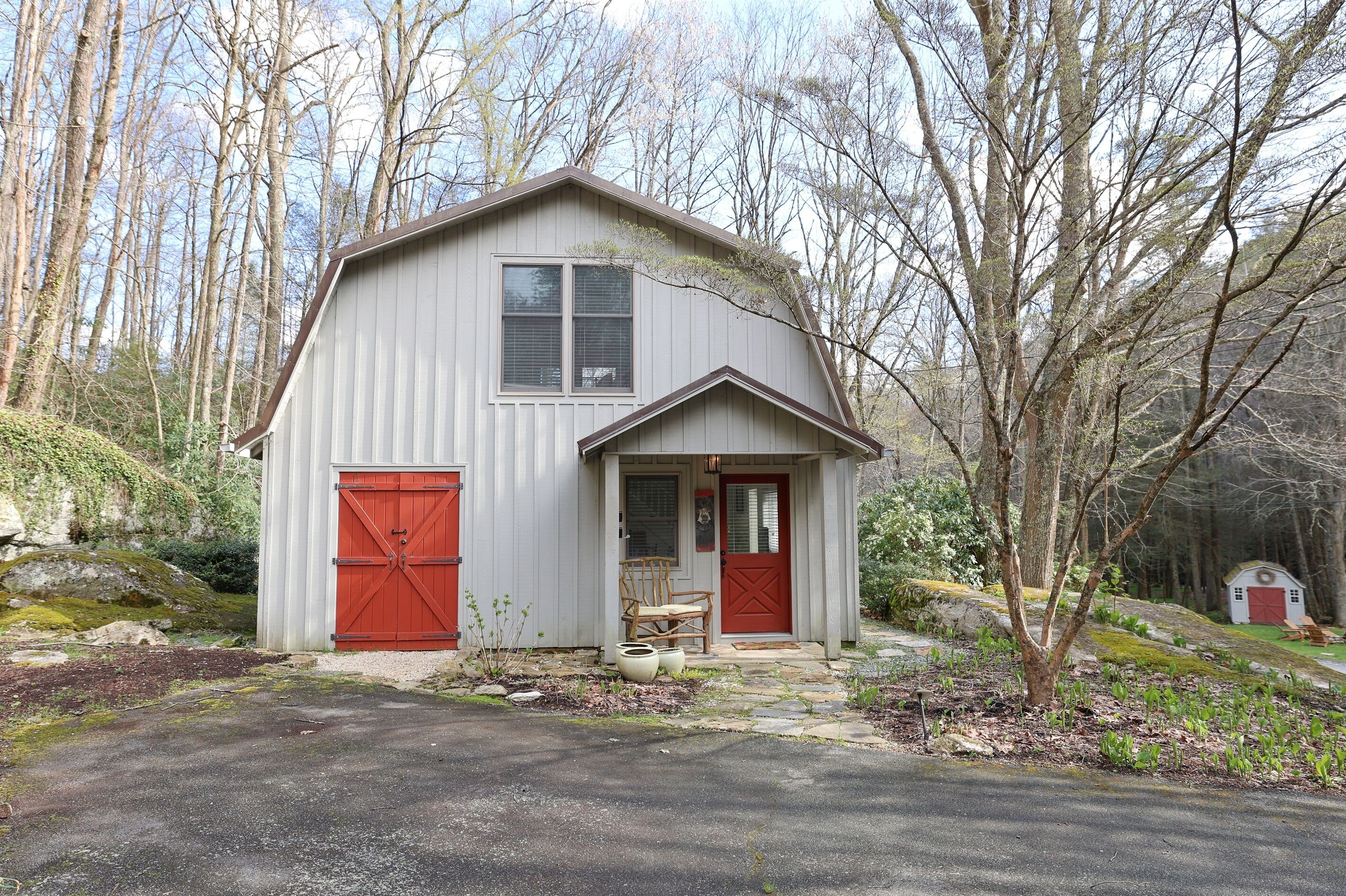 A small, single-story building with a red door and a red garage door, surrounded by trees and a stone pathway.