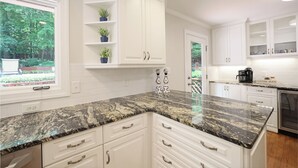 A kitchen with white cabinetry, granite countertops, and a view of greenery outside. - Lg Pool House w/ Hot Tub Central to RTP*Pool OPEN* (Durham)