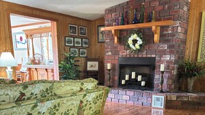 Una sala de estar con chimenea, piso de madera, un sofá floral y una pared de ladrillo.