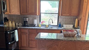 Una cocina con armarios de madera, un refrigerador de acero inoxidable, una cafetera y una ventana con vistas a la vegetación.
