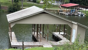 Un muelle de madera que se adentra en un lago, con una zona de estar cubierta y un edificio cercano.