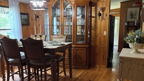 Comedor con piso de madera, una mesa de comedor de madera y sillas. Se observa un aparador de vidrio con vajilla y un candelabro sobre la mesa.