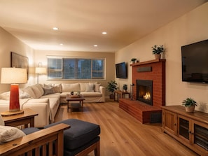 Una sala de estar con un sofá, una mesa de centro, una chimenea, un televisor y una ventana con persianas.