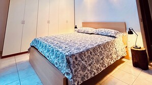 A bedroom with a skylight, a bed with patterned bedding, a wardrobe, and a bedside table with a lamp.