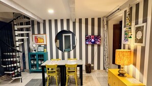 A dining area with a striped wall, a round mirror, a TV, and a yellow cabinet.