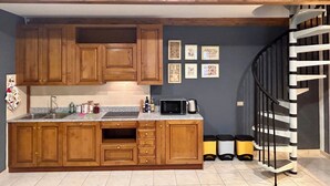 A kitchen with wooden cabinets, a granite countertop, a sink, and a black microwave. There are framed pictures on the wall and a black spiral staircase in the background.