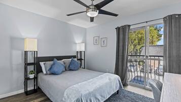A bedroom with a bed, a ceiling fan, a nightstand with a lamp, and a view through a window.