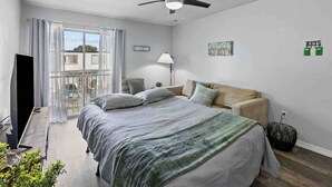 Une chambre moderne avec un lit, un ventilateur de plafond, une télévision et un balcon offrant une vue agréable.