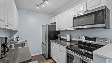 A modern kitchen with stainless steel appliances, white cabinetry, and a granite countertop.