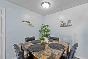 Een eetkamer met een vierkante tafel, zwarte lederen stoelen, een kamerplant en borden aan de muur.