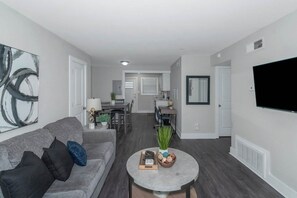 A modern living room with a grey sofa, a coffee table with decorative items, and a flat-screen TV mounted on the wall. - Central Buckhead 2BR apartment with king beds, full kitchen, fast Wi-Fi, and free parking — minutes from Lenox Square, Phipps Plaza, and top dining. (Atlanta)
