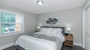 A bedroom with a bed, bedside tables, a window with blinds, a ceiling light, and a door. - Central Buckhead 2BR apartment with king beds, full kitchen, fast Wi-Fi, and free parking — minutes from Lenox Square, Phipps Plaza, and top dining. (Atlanta)