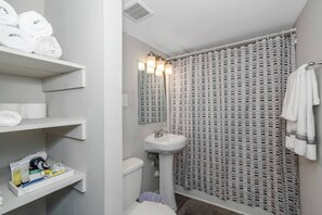A bathroom with a toilet, sink, towel rack, and shelves with toiletries. - Central Buckhead 2BR apartment with king beds, full kitchen, fast Wi-Fi, and free parking — minutes from Lenox Square, Phipps Plaza, and top dining. (Atlanta)