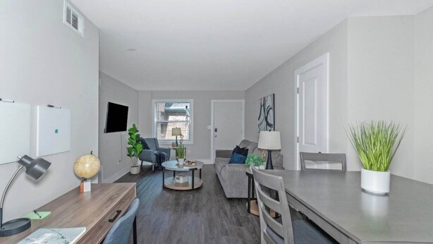 A modern living room with a sofa, a coffee table, a dining table with chairs, a TV mounted on the wall, and a potted plant. - Central Buckhead 2BR apartment with king beds, full kitchen, fast Wi-Fi, and free parking — minutes from Lenox Square, Phipps Plaza, and top dining. (Atlanta)