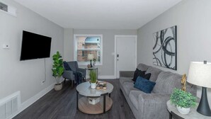 A modern living room with a flat-screen TV, grey sofa, round coffee table, and potted plants. - Central Buckhead 2BR apartment with king beds, full kitchen, fast Wi-Fi, and free parking — minutes from Lenox Square, Phipps Plaza, and top dining. (Atlanta)